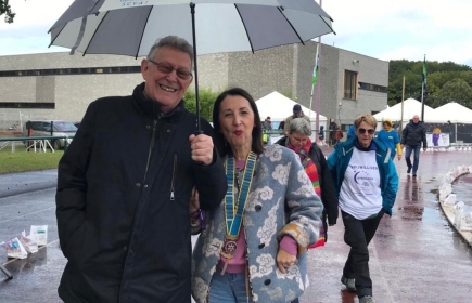 Voorzitter Ingrid samen met clublid Roger op wandel tijdens 'Levensloop Genk 2023', onder een Rotary paraplu...